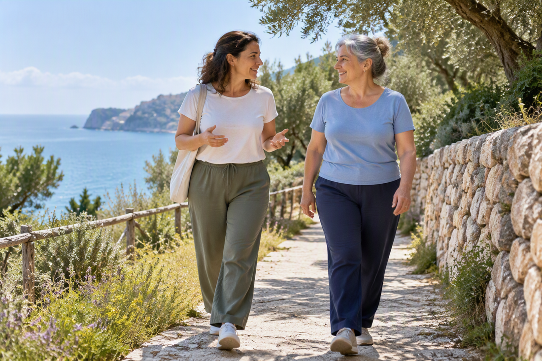 Illustrazione Copilot: due donne adulte passeggiano in un paesaggio mediterraneo immaginario, senza prodotti o risultati clinici.