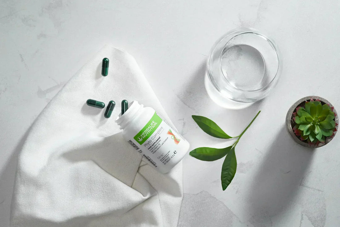 Confezione italiana Phyto Complete con capsule verdi, bicchiere d’acqua e foglie su un piano chiaro.