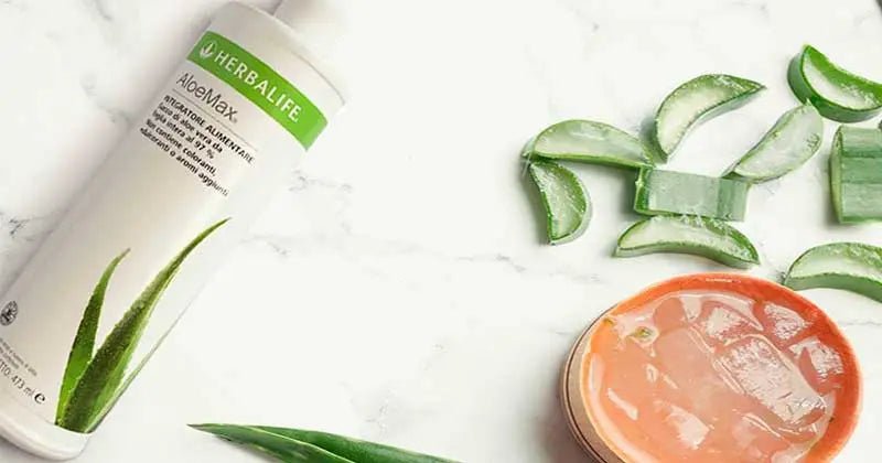 Flacone AloeMax Herbalife accanto a foglie di aloe e una bevanda