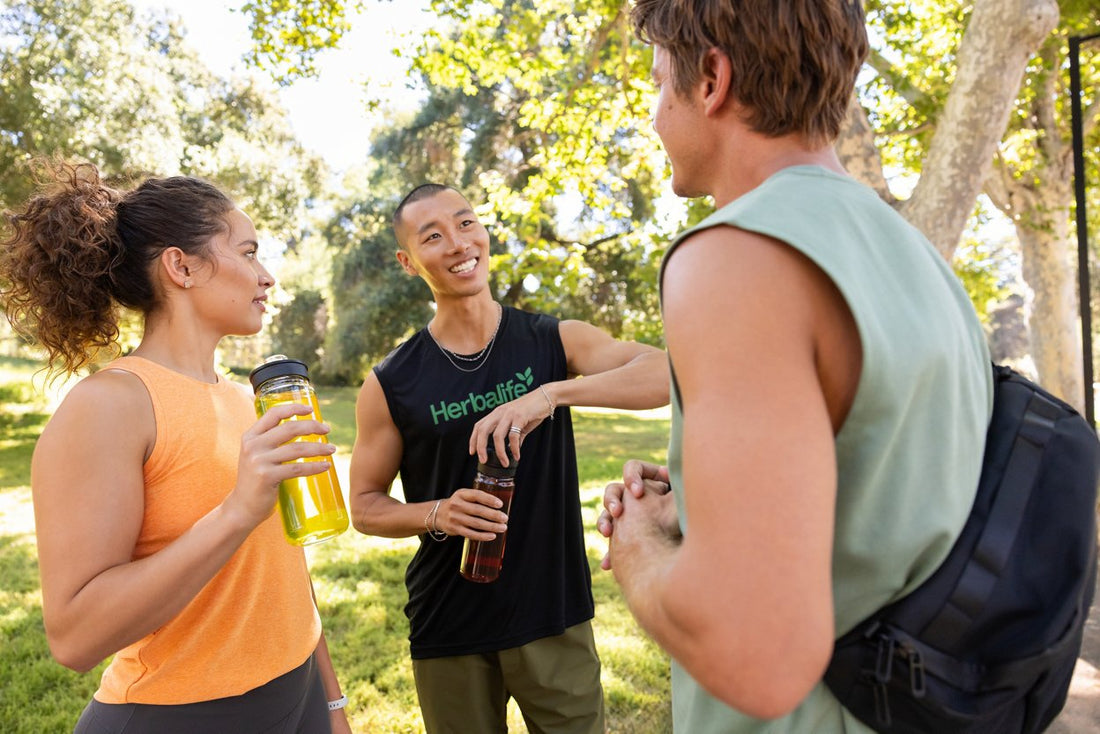 Tre persone all’aperto dopo attività fisica, con borracce e una maglia Herbalife