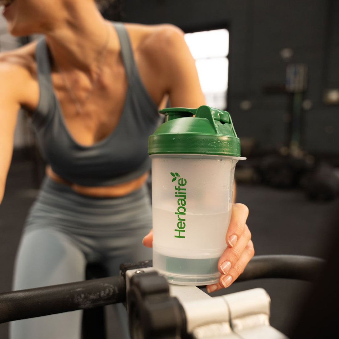 Donna in palestra con uno shaker Herbalife accanto a un attrezzo