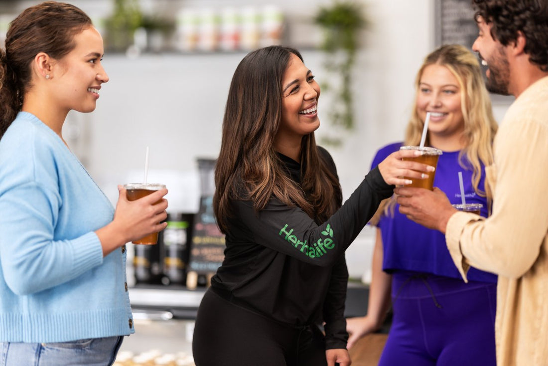 Gruppo di persone sorride e brinda in un ambiente Herbalife; una persona indossa una maglia con il marchio.