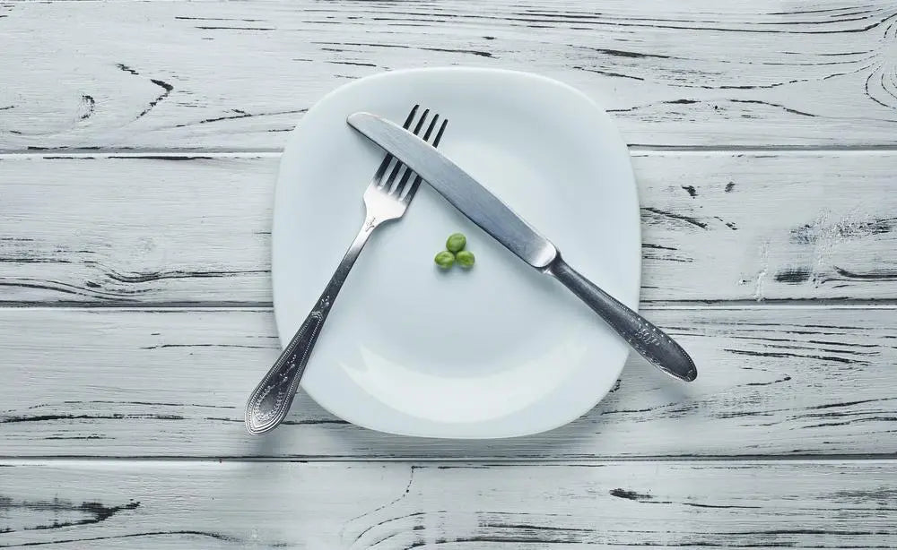 Piatto quasi vuoto con tre piselli, coltello e forchetta